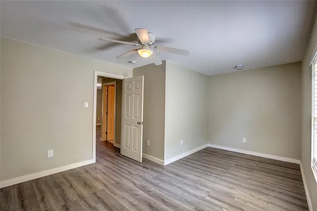 an empty room with wooden floor fan and windows