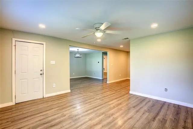 a view of an empty room with wooden floor and a ceiling fan