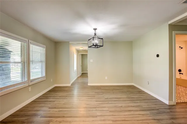 an empty room with wooden floor chandelier and windows