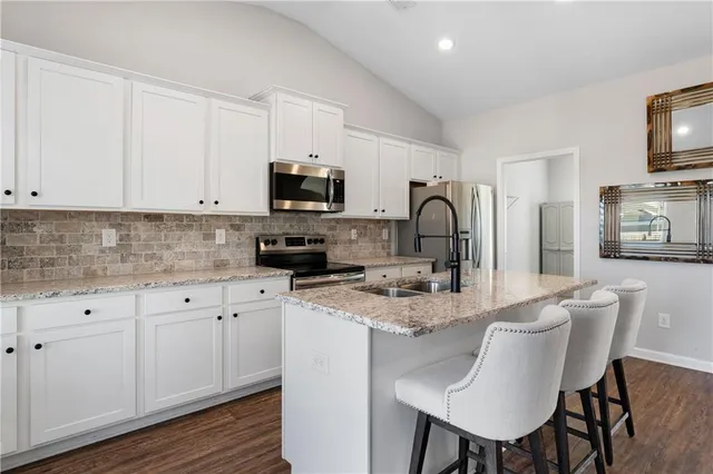 a kitchen with stainless steel appliances granite countertop a white cabinets a sink a stove a dining table and chairs with wooden floor