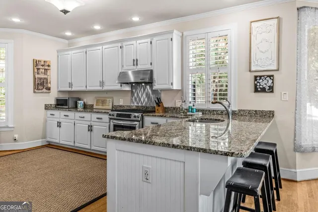 a kitchen with kitchen island granite countertop a stove a sink and white cabinets with wooden floor