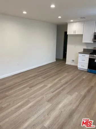 an empty room with wooden floor and kitchen view