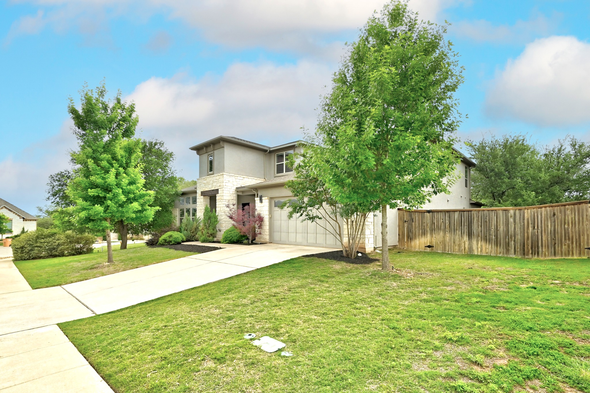 9008 Harper Rae Drive Austin, TX 78717 - Photo 3 of 39 Contemporary two-story exterior featuring a stone and stucco facade, a two-car garage, and mature trees on a manicured lawn