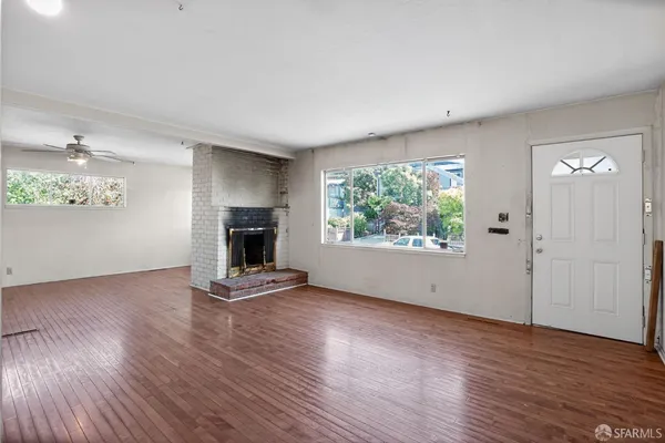 an empty room with wooden floor fireplace and windows