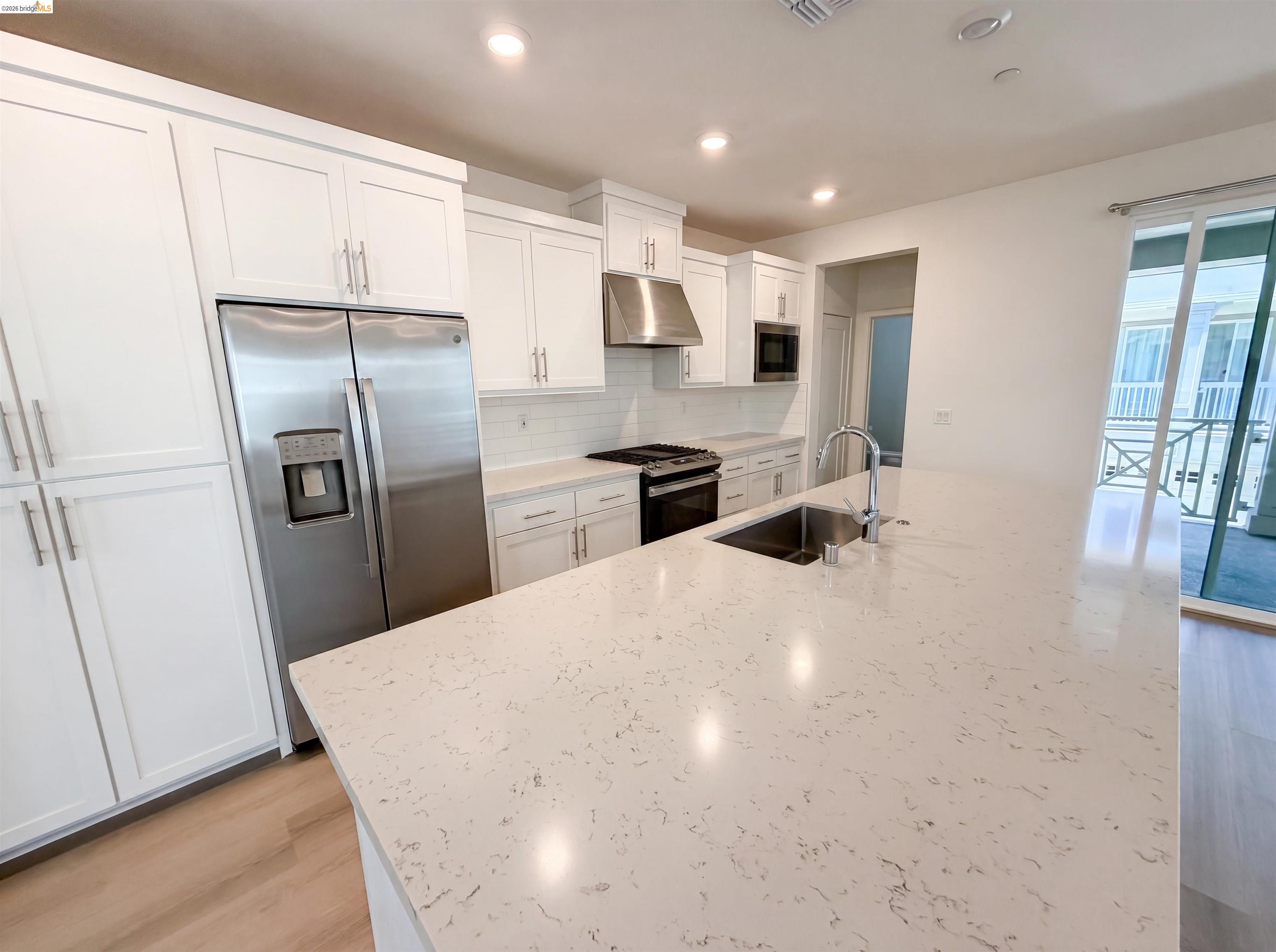 9034 Rudder Way Newark, CA 94560 - Photo 29 of 38 Kitchen featuring a large central island with an undermount sink and chrome faucet, white shaker-style cabinetry, stainless steel appliances, and wood-finish flooring