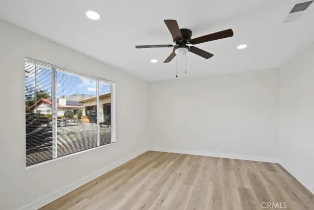a view of an empty room with wooden floor and a ceiling fan