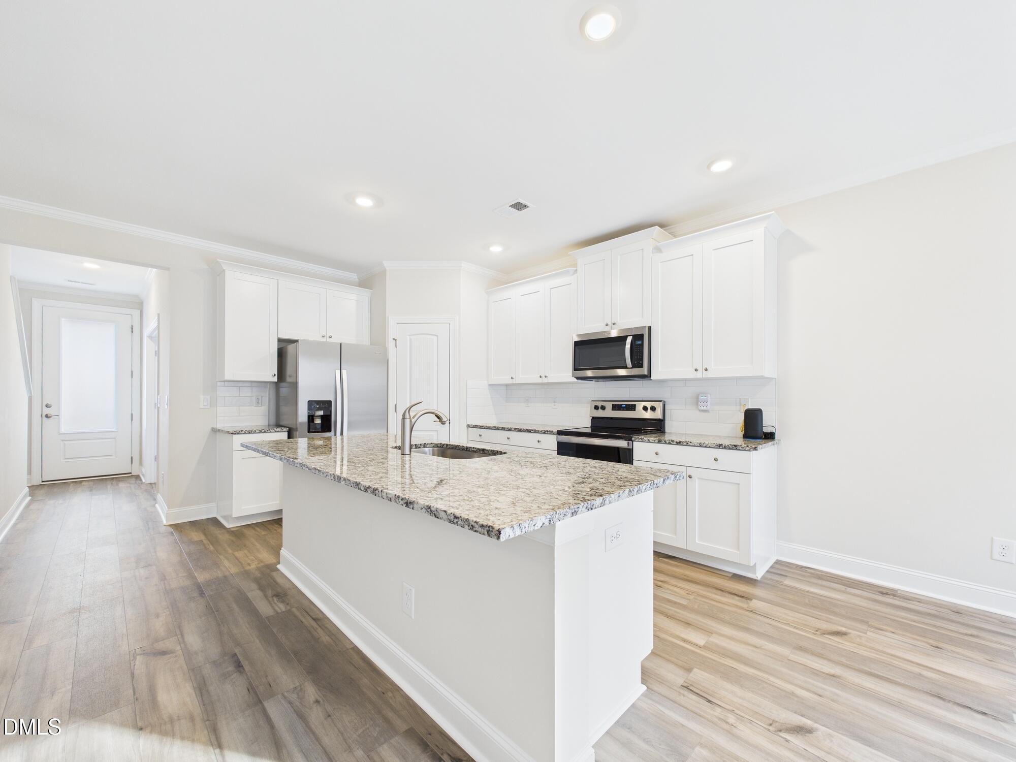 110 Symmetry Loop Youngsville, NC 27596 - Photo 20 of 72 a large white kitchen with stainless steel appliances granite countertop a stove a sink a refrigerator and white cabinets with wooden floor