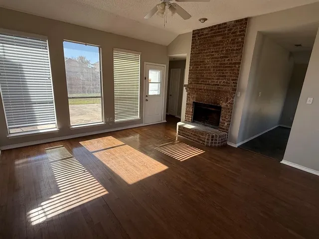 a view of an empty room with wooden floor fireplace and a window