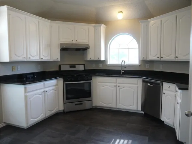 a kitchen with granite countertop white cabinets white stainless steel appliances and a sink