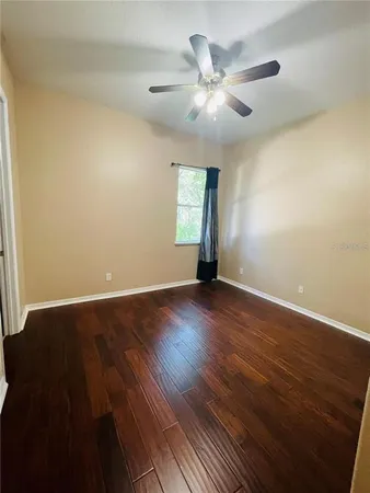 a view of an empty room with wooden floor and a ceiling fan