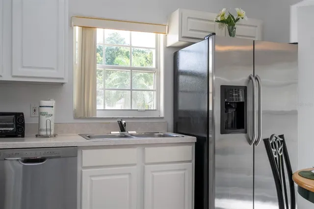 a kitchen with stainless steel appliances granite countertop a refrigerator a sink a stove and white cabinets with wooden floor