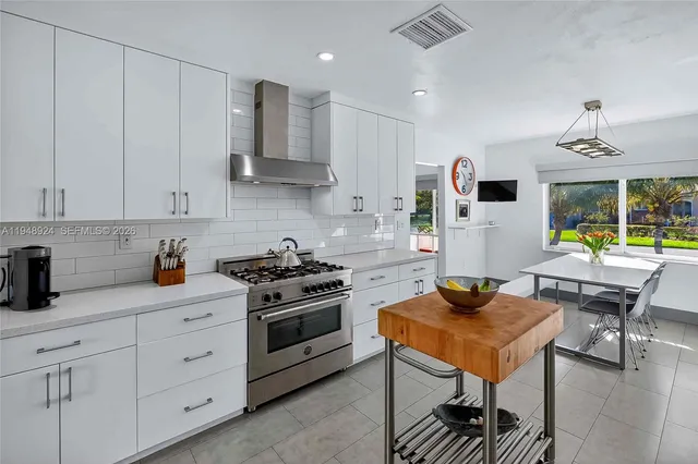 a kitchen with stainless steel appliances granite countertop a stove a sink dishwasher and white cabinets with wooden floor