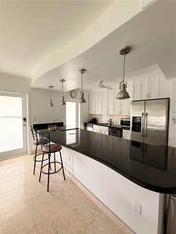 a kitchen with stainless steel appliances kitchen island granite countertop a refrigerator a stove a sink a dining table and chairs with wooden floor