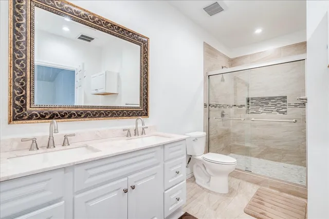 a bathroom with a double vanity sink mirror double shower and a toilet