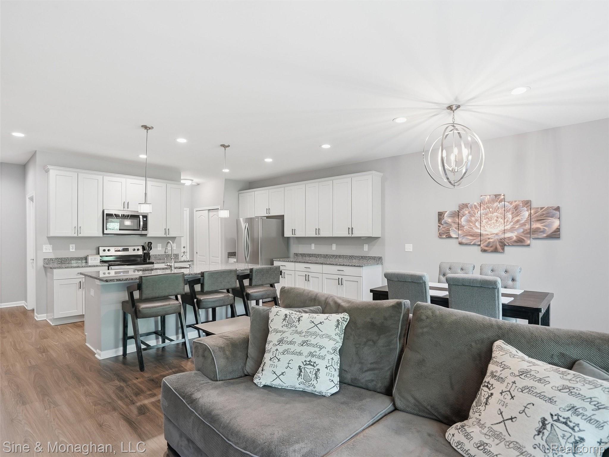 24827 Ivy Road Novi, MI 48375 - Photo 12 of 38 Open-concept living area featuring wood-finish flooring, a kitchen with white cabinetry and stainless steel appliances, a kitchen island with seating, pendant lighting, and recessed ceiling lights