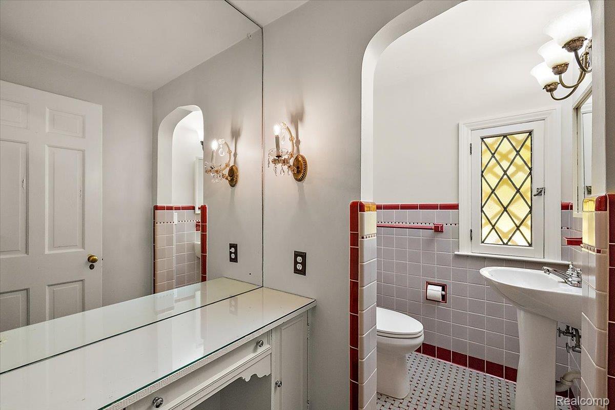1051 Devonshire Road Grosse Pointe, MI 48230 - Photo 24 of 99 Bathroom featuring a decorative leaded glass window, pedestal sink, ceramic tile wainscoting with a red trim, and dual wall sconces