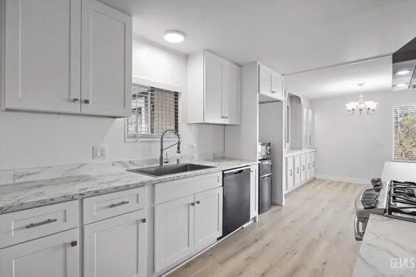 a kitchen with a sink dishwasher a stove and white cabinets with wooden floor