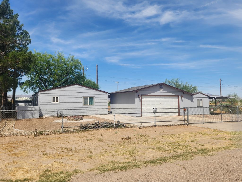 Single-story residence featuring a two-car garage , a paved driveway, attached covered carport and chain-link fencing with roll gate and double gate entry
