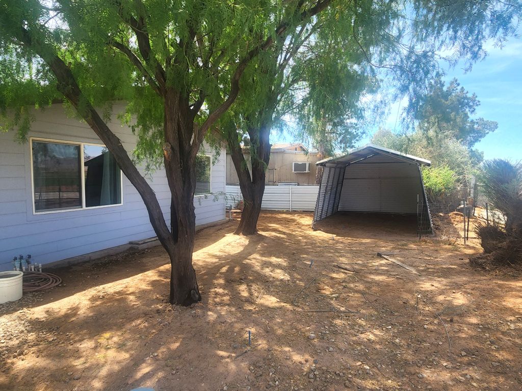 8257 Green Valley Road Mohave Valley, AZ 86440 - Photo 14 of 41 Side yard featuring established trees, an open shed, and horizontal wood siding with white-framed windows