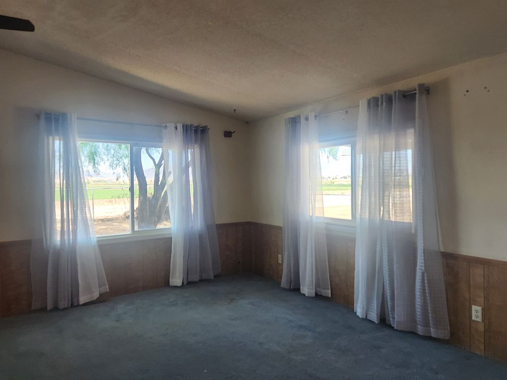 8257 Green Valley Road Mohave Valley, AZ 86440 - Photo 19 of 41 Room featuring two large windows, wood-panel wainscoting, and carpet flooring