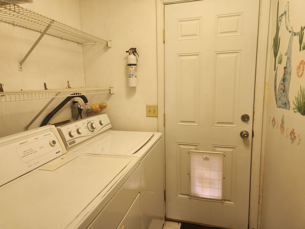 8257 Green Valley Road Mohave Valley, AZ 86440 - Photo 26 of 41 Dedicated laundry area featuring a top-loading washer and dryer set, white wire shelving, and a paneled entry door with a pet door
