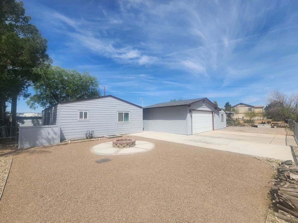 8257 Green Valley Road Mohave Valley, AZ 86440 - Photo 5 of 41 Spacious gravel yard featuring a stone-clad fire pit with a concrete surround, a detached garage with a white roll-up door, and the side of the house featuring horizontal wood siding and multiple windows