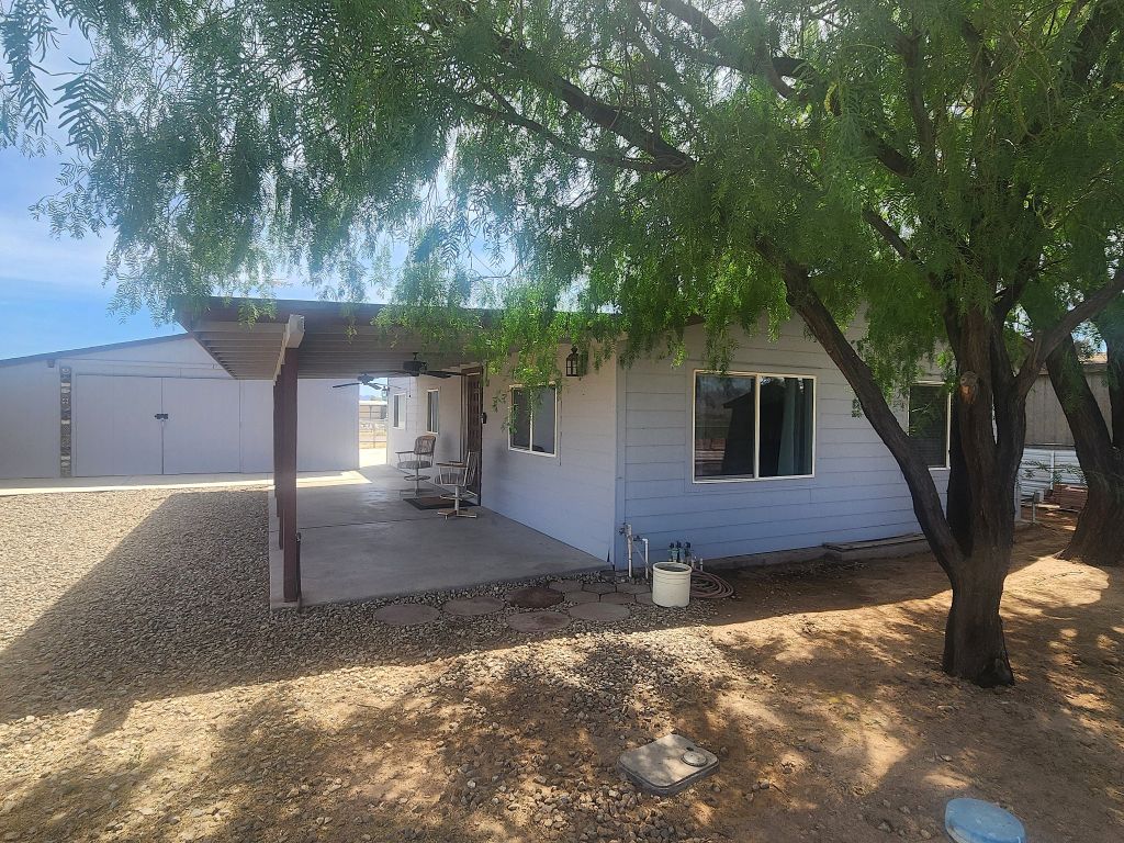 8257 Green Valley Road Mohave Valley, AZ 86440 - Photo 9 of 41 Exterior featuring wood siding, a covered patio with ceiling fans, a gravel yard, and mature trees