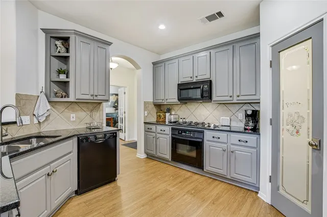 a kitchen with stainless steel appliances granite countertop a stove top oven a sink dishwasher and a refrigerator with wooden cabinets