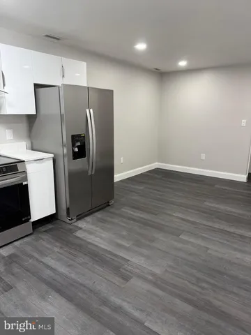 a view of a refrigerator in kitchen and an empty room with wooden floor