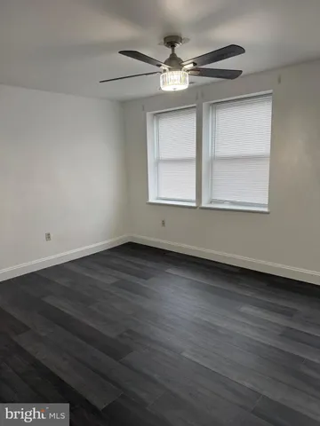 an empty room with wooden floor chandelier fan and windows