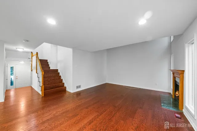 a view of an empty room with wooden floor fireplace and a window