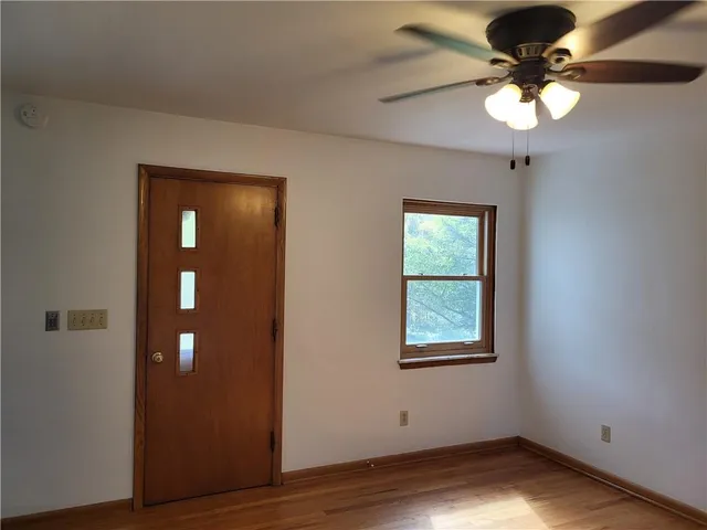 a view of an empty room with wooden floor and a chandelier fan