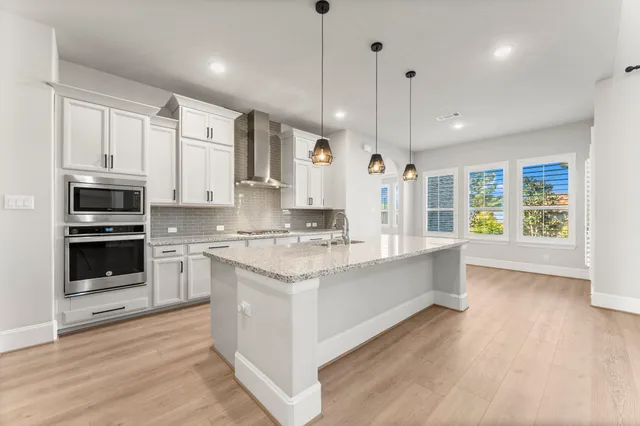 a large kitchen with stainless steel appliances kitchen island granite countertop a stove a sink a refrigerator and white cabinets with wooden floor