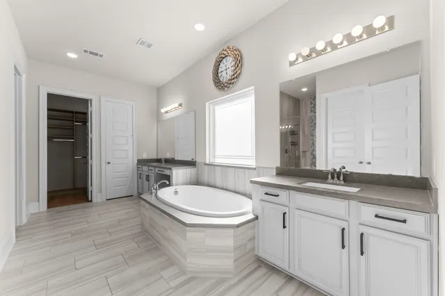 a spacious bathroom with a granite countertop double vanity sink a mirror and a bathtub