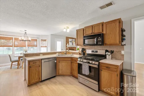 a kitchen with stainless steel appliances granite countertop a stove top oven a sink dishwasher a dining table and chairs with wooden floor