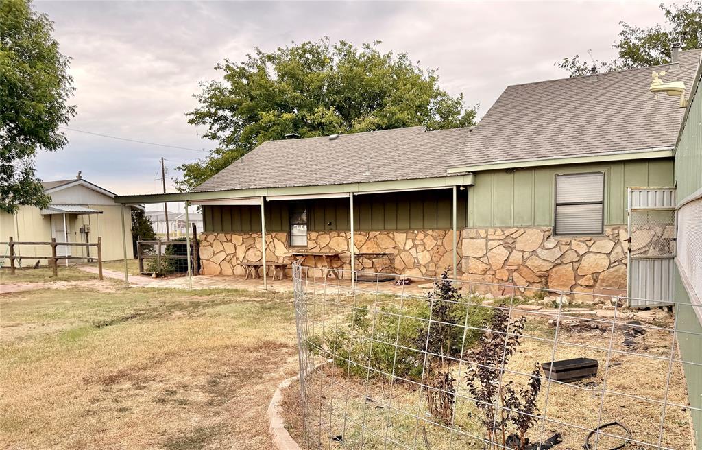 504 Loop Road Quanah, TX 79252 - Photo 5 of 40 Back of house featuring a shingled roof, stone siding, and a vegetable garden