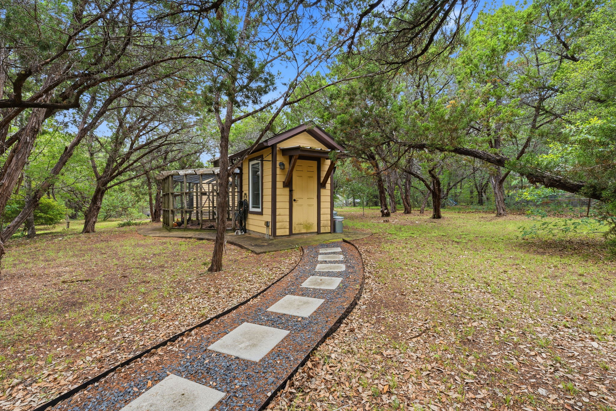 8121 Bluff Trail Austin, TX 78737 - Photo 35 of 40 A quaint yellow outbuilding sits nestled among mature trees, with a charming stepping stone pathway leading to its entrance.