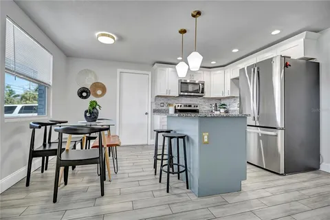 a kitchen with stainless steel appliances granite countertop a refrigerator a sink dishwasher a stove and a dining table with wooden floor