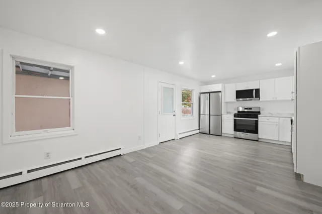 an empty room with wooden floor kitchen view and a window