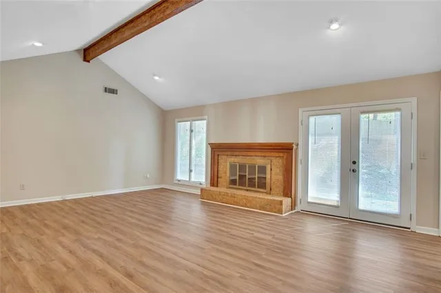 an empty room with wooden floor fire place and windows