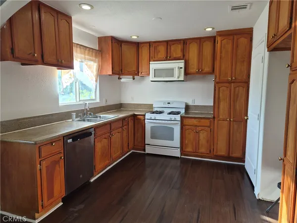 a kitchen with stainless steel appliances granite countertop wooden cabinets a sink a stove a refrigerator and island with wooden floor