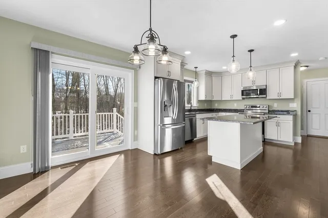 a kitchen with stainless steel appliances kitchen island granite countertop a refrigerator a oven a large island with wooden floor and cabinets