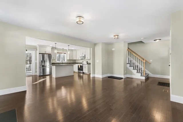 a view of an empty room with wooden floor and a kitchen