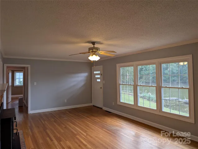 a view of an empty room with wooden floor fireplace and a window