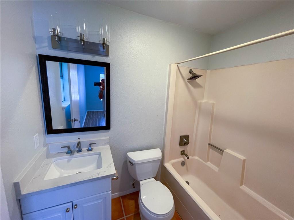 2102 Kenneth Avenue, Unit A Austin, TX 78741 - Photo 11 of 15 Bathroom featuring a white vanity with a rectangular sink and stone-finish countertop, a rectangular mirror with a dark frame, a three-light vanity fixture, a toilet, and a combination shower/bathtub unit