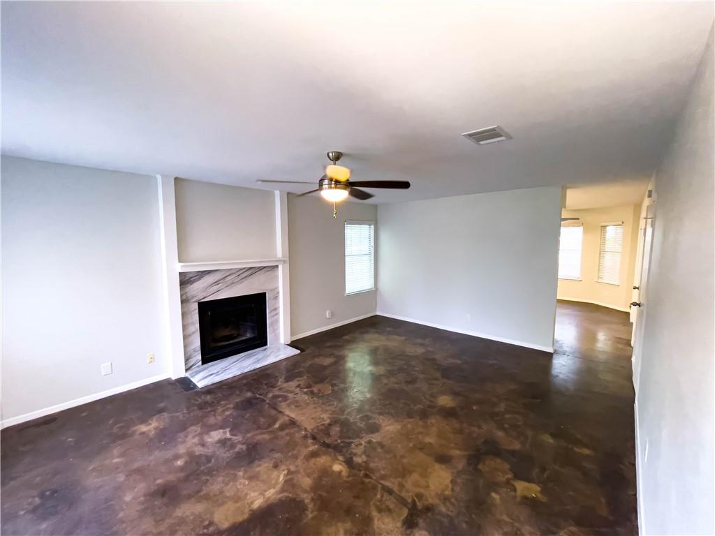 2102 Kenneth Avenue, Unit A Austin, TX 78741 - Photo 4 of 15 Living area featuring a fireplace with a stone surround, a ceiling fan, windows providing natural light, and stained concrete flooring