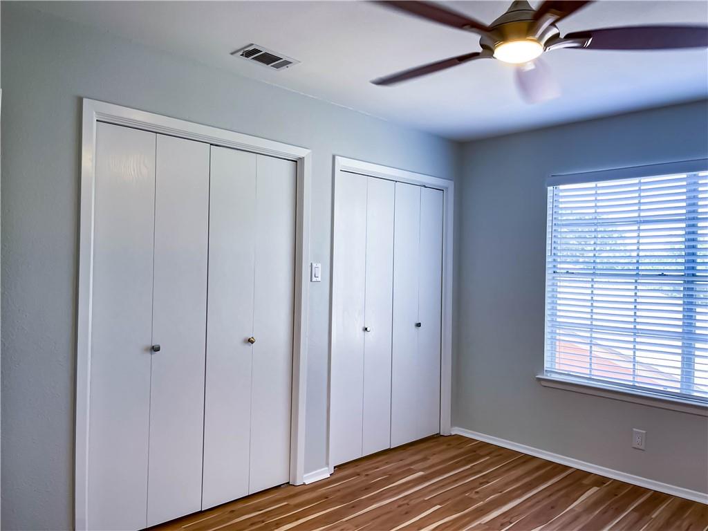 2102 Kenneth Avenue, Unit A Austin, TX 78741 - Photo 10 of 15 Room featuring two sets of bi-fold closet doors, wood-finish flooring, a window with horizontal blinds, and a ceiling fan with integrated lighting