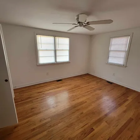 an empty room with wooden floor fan and windows