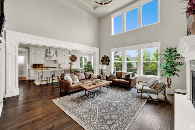 1132 South 1300th Street West Mapleton, UT 84664 - Photo 5 of 52 Spacious open-concept living area featuring rich wood-finish flooring, a two-story ceiling, multiple large windows, and a prominent fireplace with a substantial white mantel