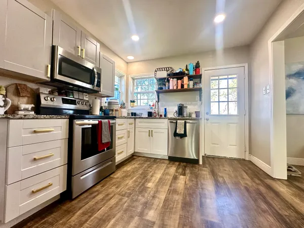 a white kitchen with stainless steel appliances granite countertop a stove and a sink